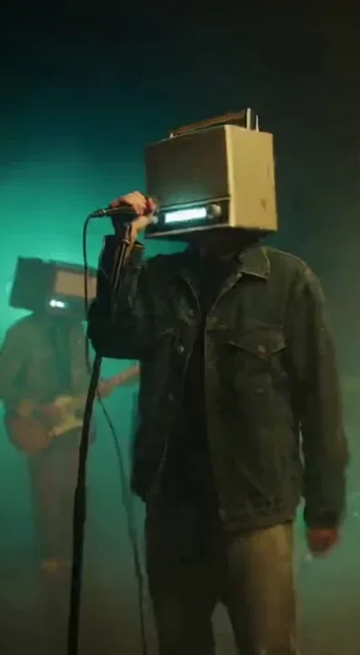 A surreal music video featuring a melancholic alternative-rock band where each member has an old analog radio instead of a head. The singer’s radio flickers with static as he sings, the guitarist’s antenna shakes with emotion, and the drummer’s radio glows red during intense moments. The song has a dreamy, experimental sound with layered vocals, glitchy beats, and moody guitar riffs. The stage is dim, foggy, and bathed in vintage green and amber lighting. Cameras drift slowly around the band. Emotional, existential tone — themes of alienation and digital decay. No direct references to real musicians.
